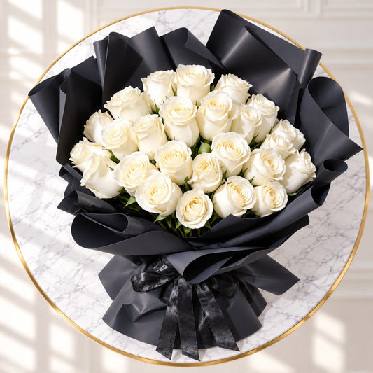 A round bouquet of white roses wrapped in black paper and ribbon, displayed on a round marble table with a gold rim.