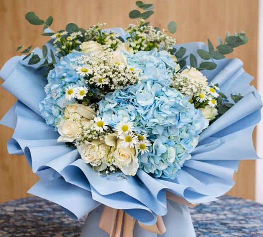 Bouquet of flowers wrapped in blue paper on a wooden surface