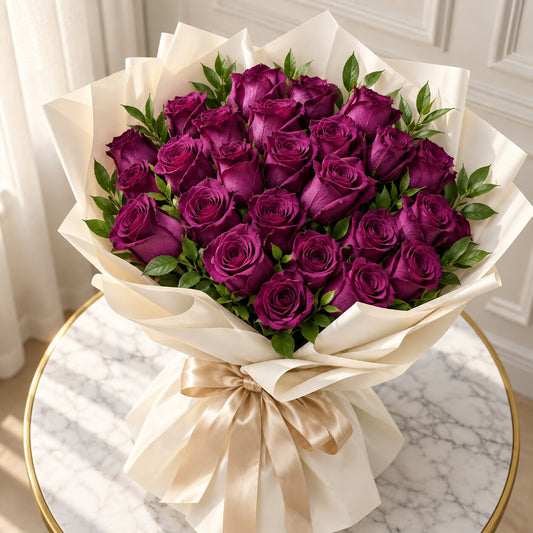 A large bouquet of deep purple roses wrapped in cream paper with a beige satin bow, displayed on a marble-topped table.
