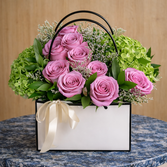 Floral arrangement with pink roses and green hydrangeas in a decorative box on a marble surface.