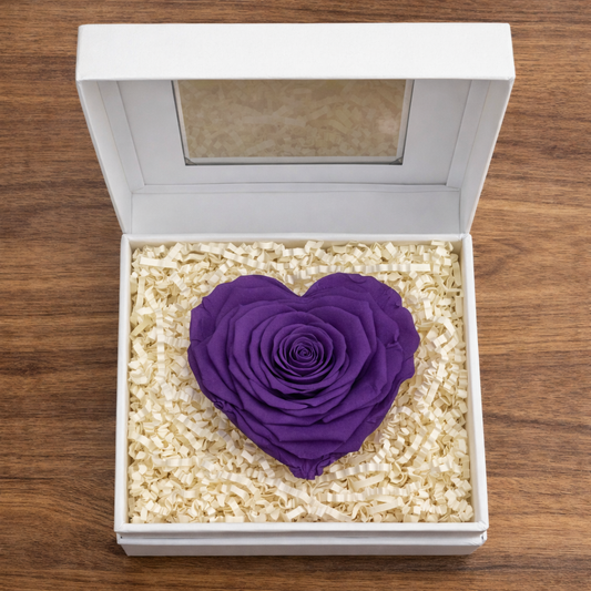 Purple preserved rose heart in an open gift box with decorative filler.
