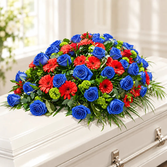 Blue roses with red gerberas and lush green foliage in the Scarlet Ember Memorial funeral arrangement.
