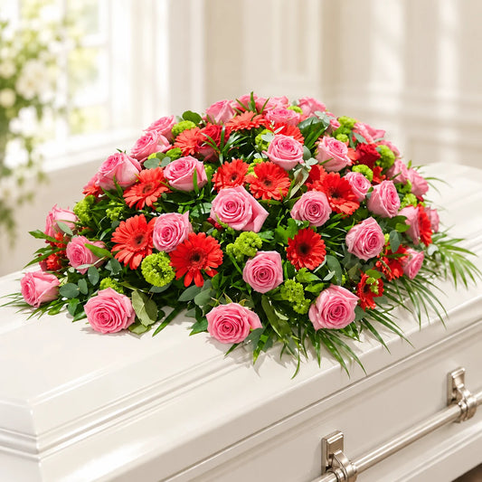 Pink rose casket spray with red gerberas and green floral accents on an ivory-white casket.