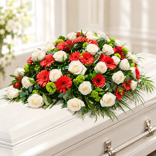 White rose casket spray with red gerberas, green chrysanthemums and flowing foliage on an ivory casket.